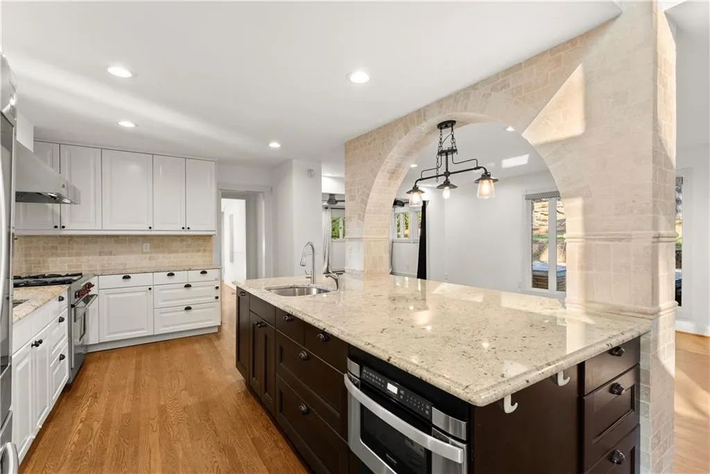 Kitchen featuring white cabinets, decorative light fixtures, light wood-style floors, light stone counters, and tasteful backsplash