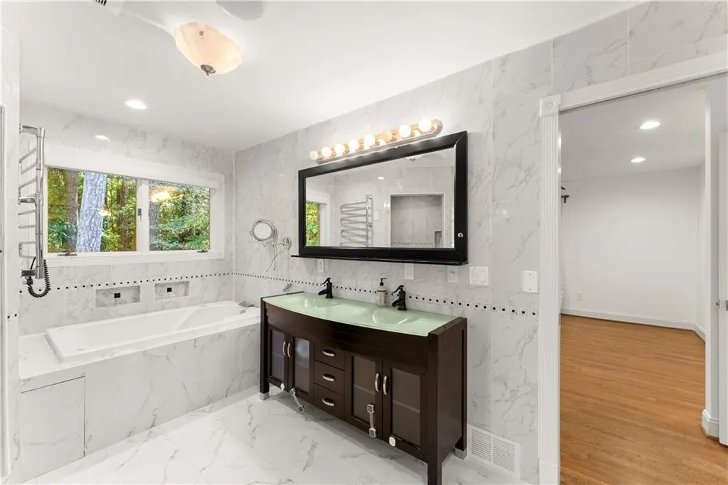 Bathroom with tile walls, a bath, double vanity, light marble finish flooring, and a towel warming rack