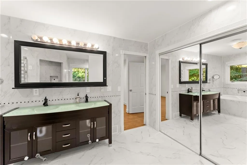 Bathroom featuring double vanity, a garden tub, light marble finish floors, and tile walls