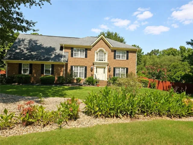 Brick exterior, arched entryway, gabled roof, white-trimmed windows with black shutters, and mature landscaping