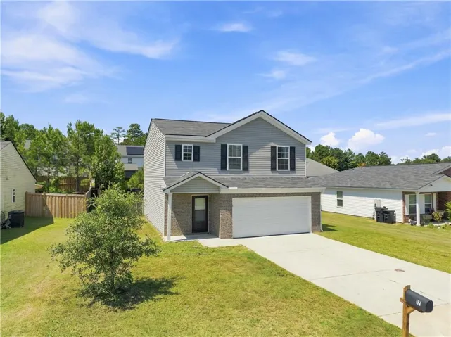 Two-story residence featuring grey siding, dark shutters, an attached garage, a concrete driveway, and a partially fenced yard