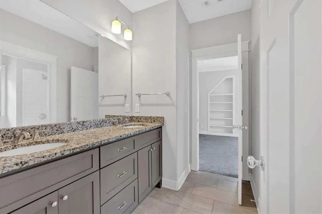 Bathroom with double vanity, a spacious closet, tile patterned flooring, and a tile shower