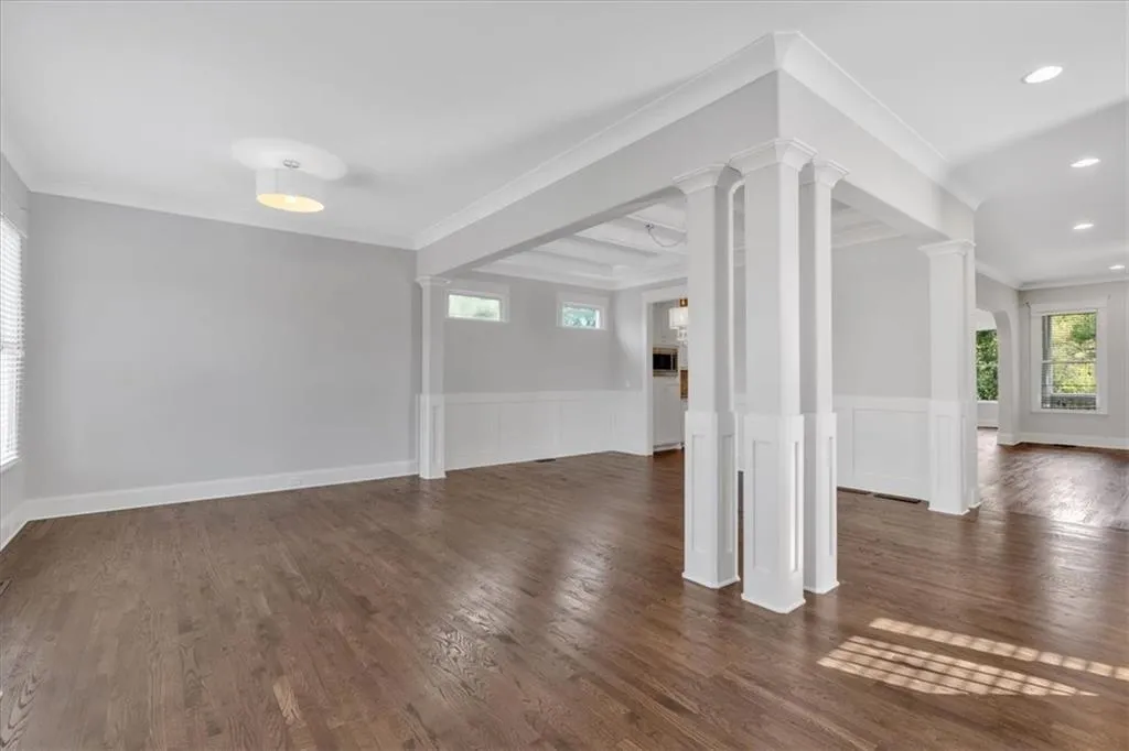 Unfurnished room with decorative columns, wainscoting, dark wood-style floors, ornamental molding, and recessed lighting
