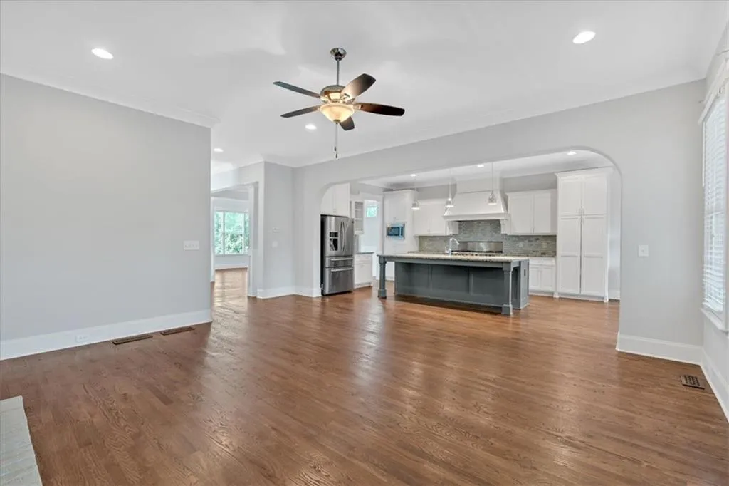 Unfurnished living room featuring arched walkways, ceiling fan, recessed lighting, dark wood finished floors, and ornamental molding