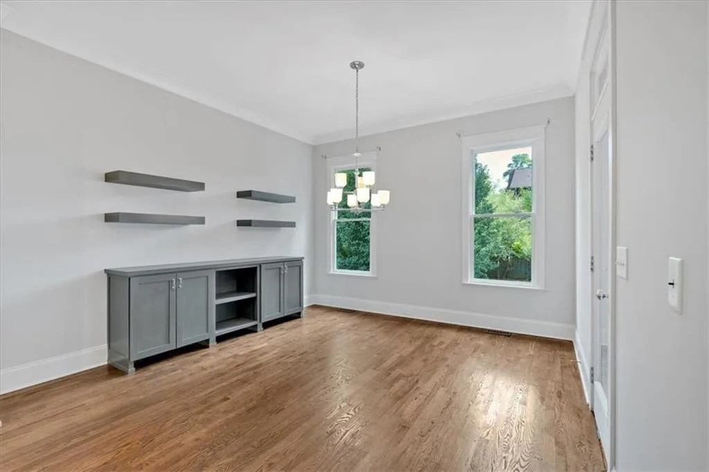 Unfurnished living room featuring a chandelier, wood finished floors, and crown molding