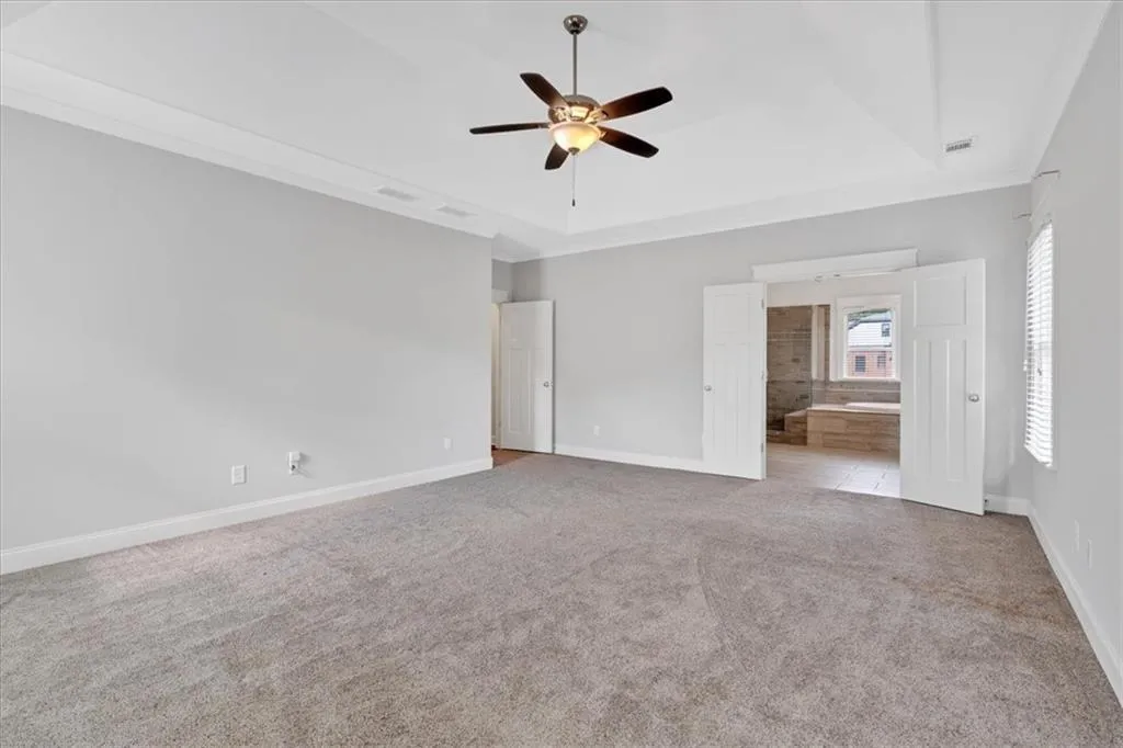 Unfurnished bedroom featuring carpet, a tray ceiling, connected bathroom, and ceiling fan