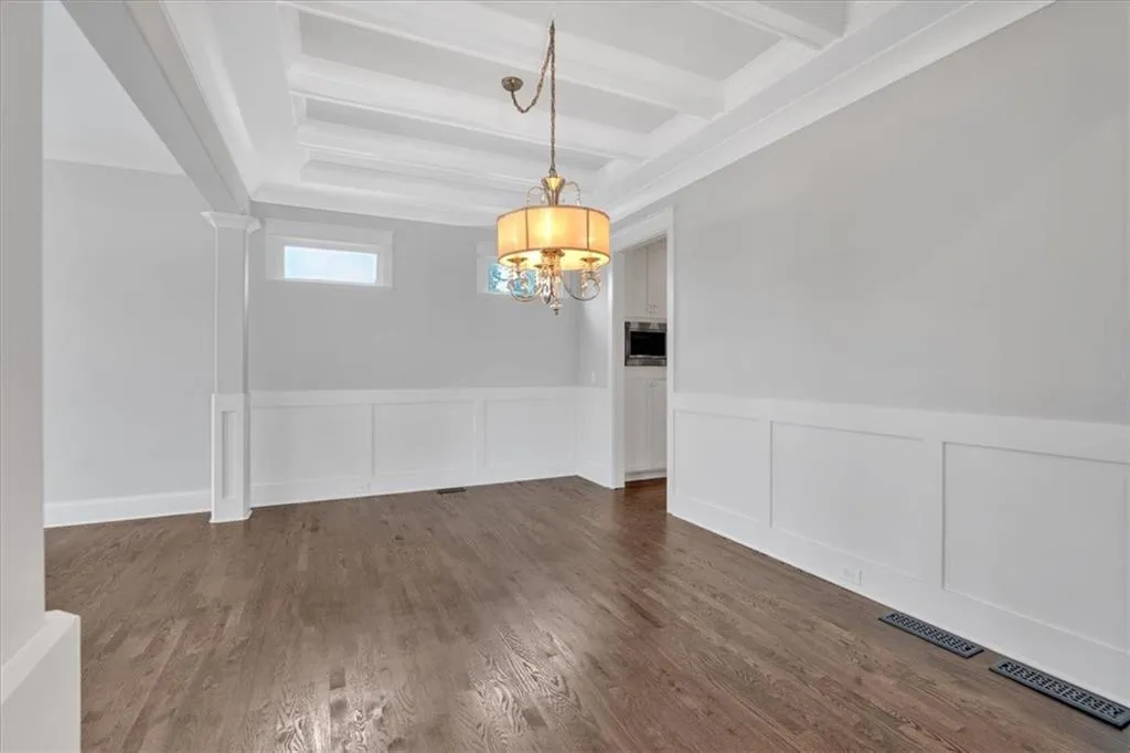 Unfurnished dining area featuring beamed ceiling, a chandelier, dark wood-style flooring, wainscoting, and a decorative wall