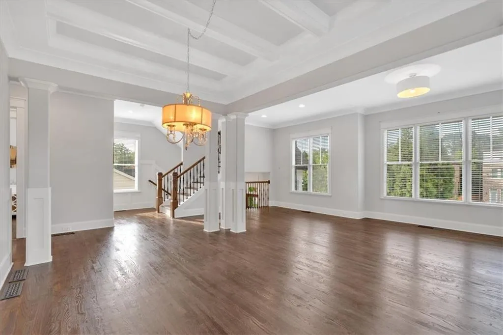 Unfurnished living room with ornate columns, wood finished floors, beam ceiling, stairs, and recessed lighting