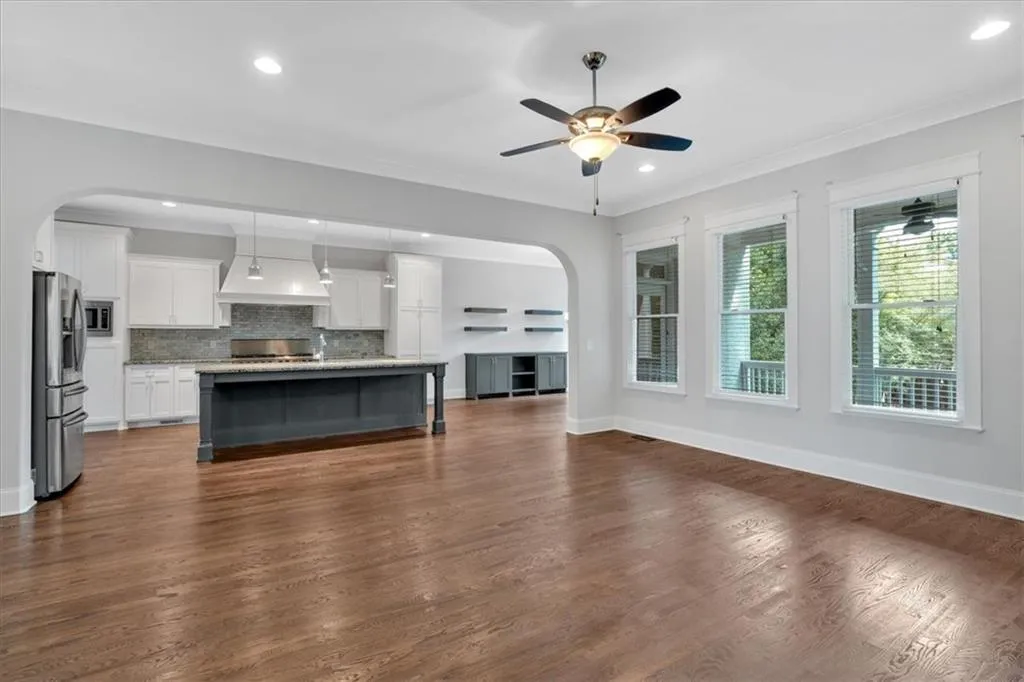 Unfurnished living room featuring arched walkways, ceiling fan, dark wood finished floors, recessed lighting, and ornamental molding