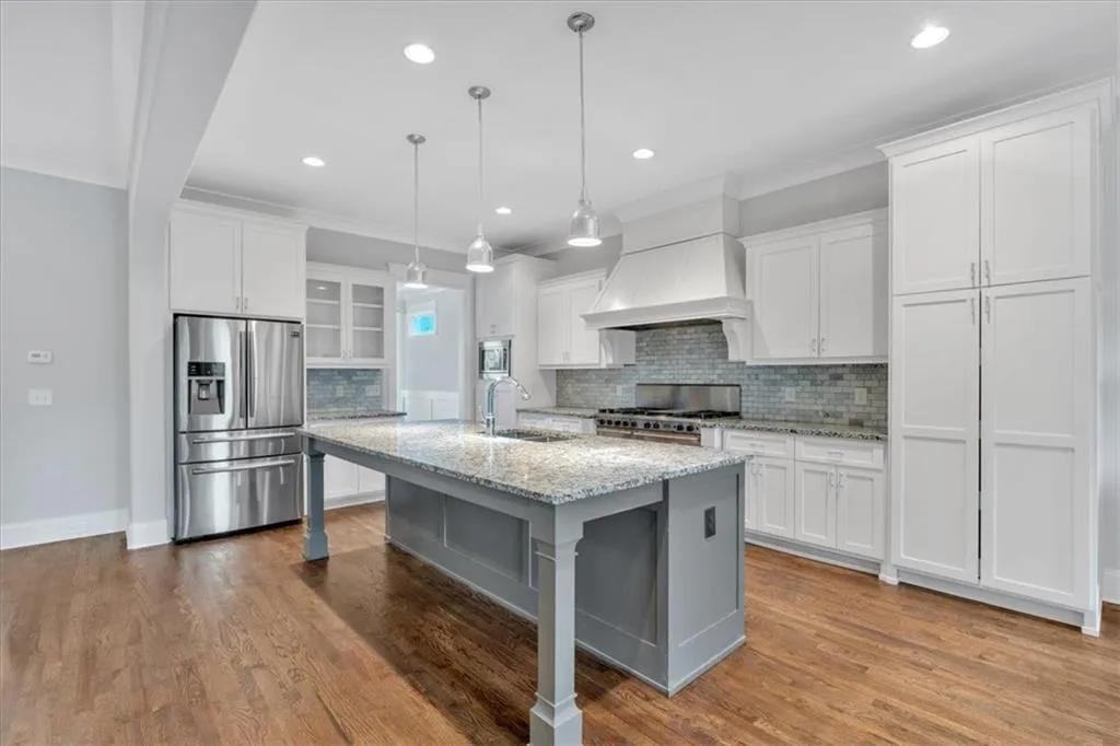 Kitchen featuring stainless steel refrigerator with ice dispenser, stove, custom exhaust hood, backsplash, and white cabinets
