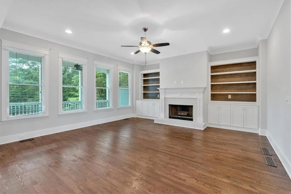 Unfurnished living room with a ceiling fan, crown molding, plenty of natural light, built in features, and a fireplace