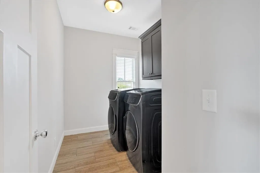 Laundry area featuring washing machine and dryer, cabinet space, and light wood-type flooring
