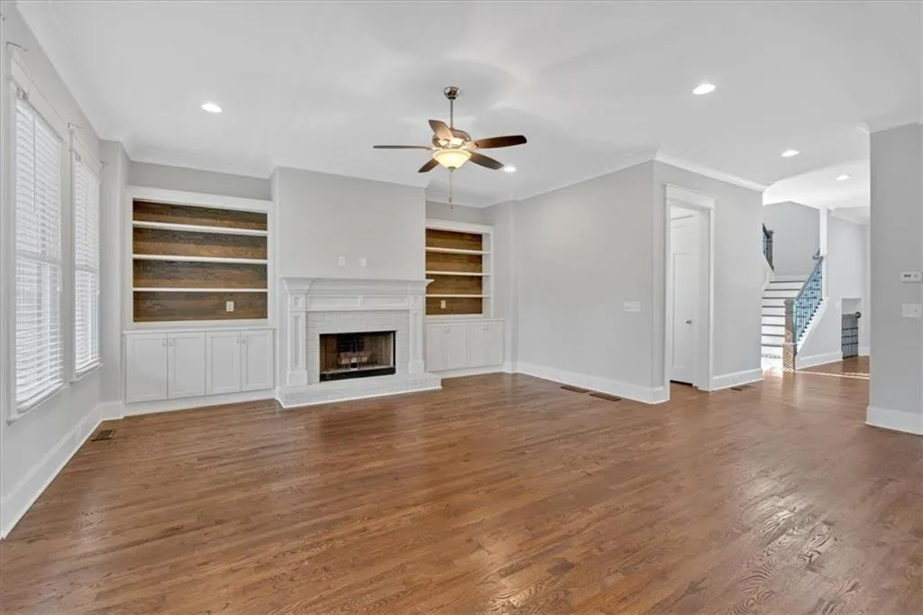Unfurnished living room with a ceiling fan, stairs, crown molding, built in features, and a brick fireplace