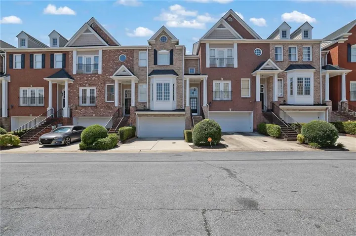 Brick and stone facade townhome with covered entry, attached garage, and dormer windows