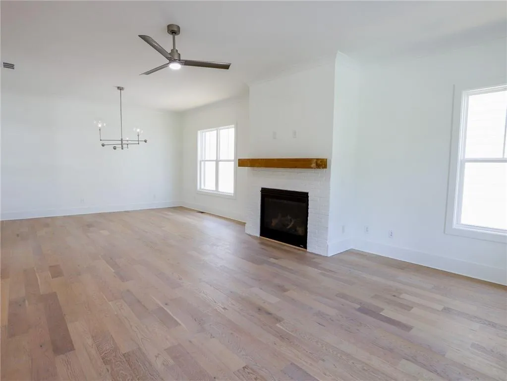 Unfurnished living room with a ceiling fan, a chandelier, a brick fireplace, light wood finished floors, and crown molding