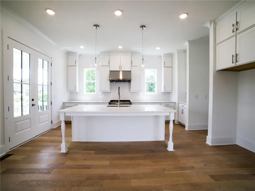 Kitchen with an island with sink, under cabinet range hood, white cabinets, a breakfast bar area, and recessed lighting