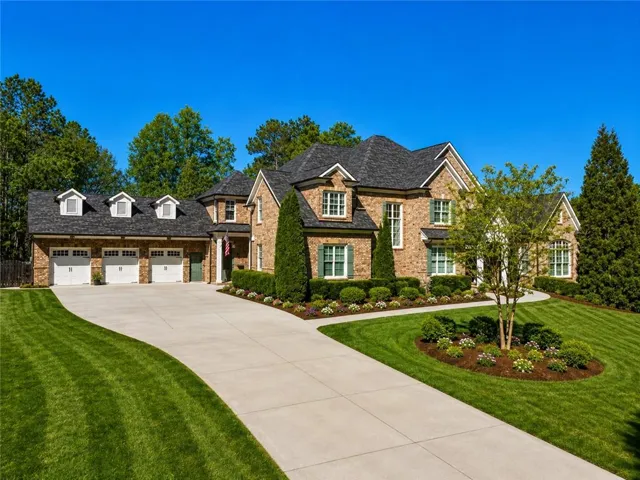Brick facade residence featuring a three-car garage with dormer windows, a concrete driveway, and established landscaping