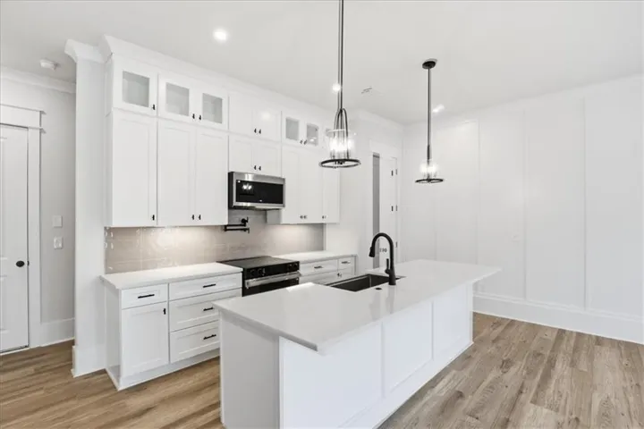 Contemporary kitchen featuring white cabinetry, a large center island with a built-in sink, stainless steel appliances, and sleek pendant lighting