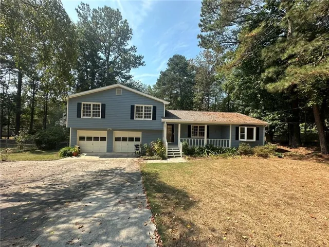Split-level residence featuring a two-car garage, front porch with white railing, and a mature tree canopy