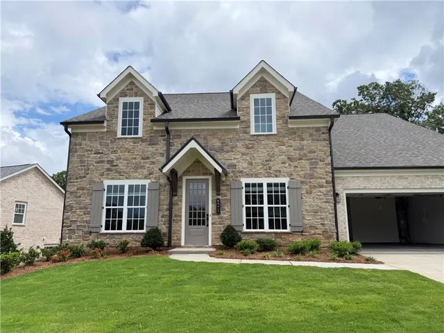 Stone facade residence featuring a two-car garage, dormer windows, decorative shutters, a covered entry, and manicured landscaping