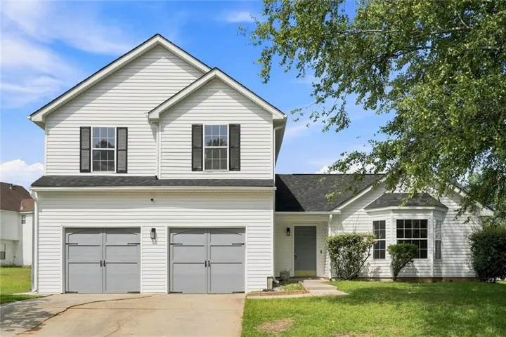 Two-story exterior with white siding, black window shutters, a two-car garage, and a bay window