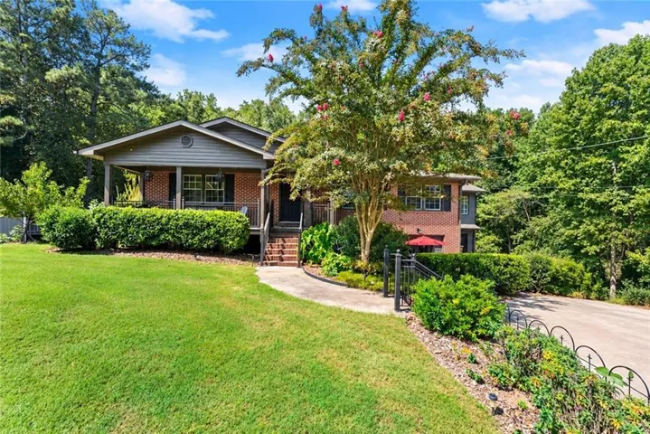 Brick and siding exterior with a covered front porch, established landscaping, mature trees, and a paved driveway