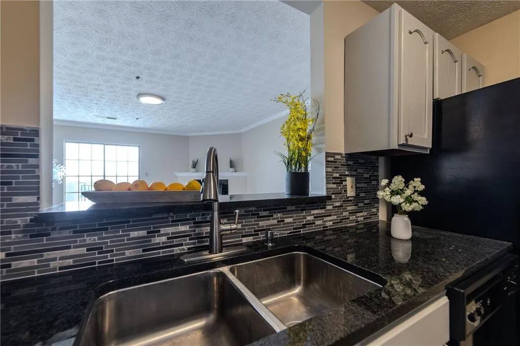 Kitchen featuring ornamental molding, dark stone countertops, backsplash, black dishwasher, and white cabinets