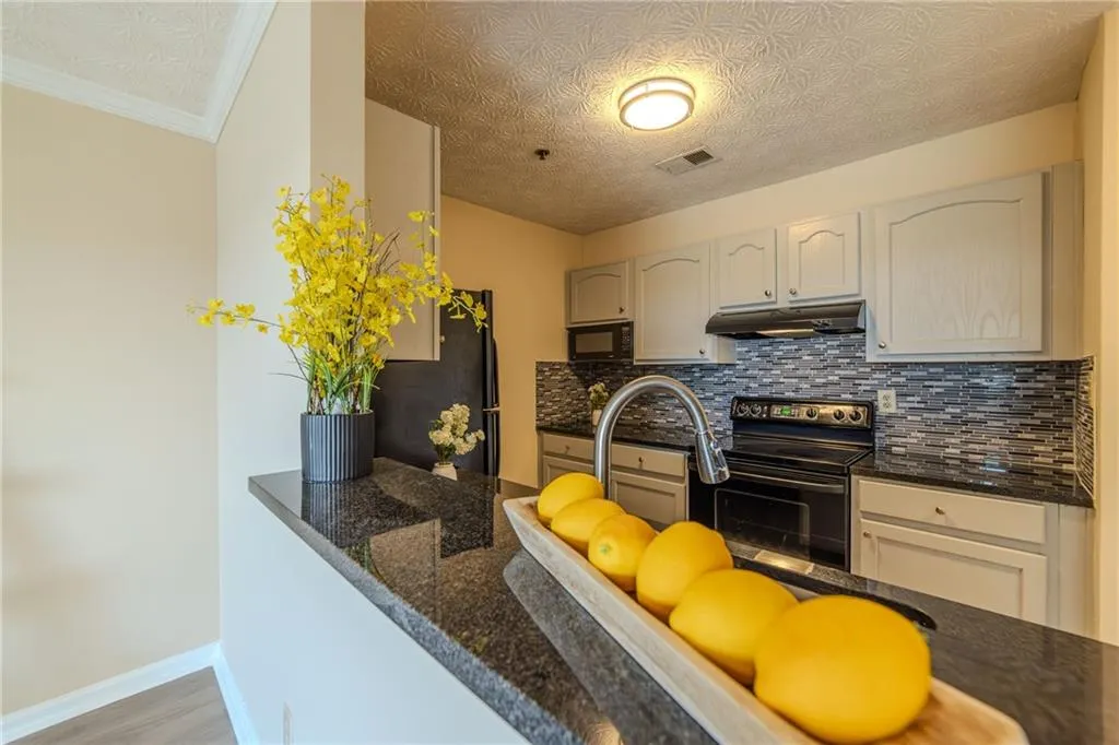Kitchen featuring black appliances, under cabinet range hood, decorative backsplash, and dark stone countertops