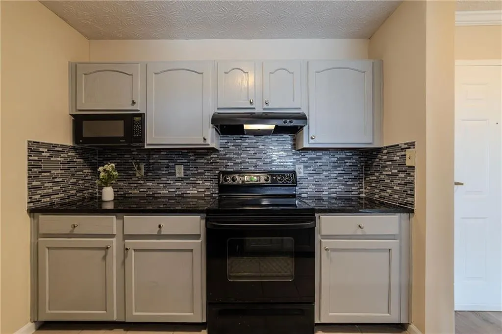 Kitchen featuring black appliances, under cabinet range hood, backsplash, a textured ceiling, and dark stone counters
