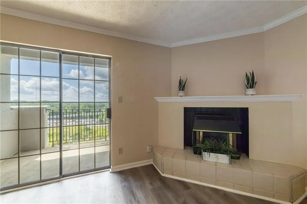Unfurnished living room with a textured ceiling, wood finished floors, crown molding, and a glass covered fireplace