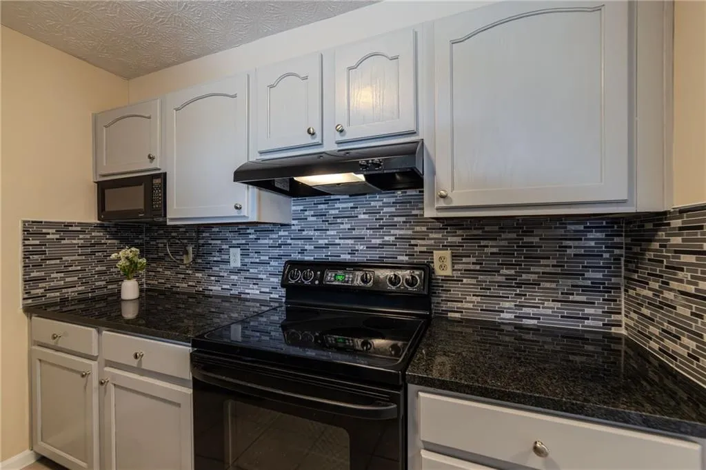 Kitchen with black appliances, under cabinet range hood, backsplash, and dark stone counters