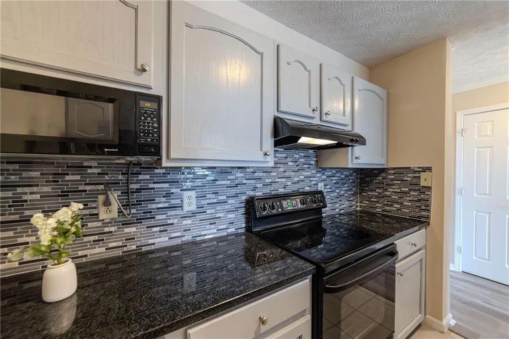 Kitchen featuring black appliances, a textured ceiling, under cabinet range hood, tasteful backsplash, and crown molding