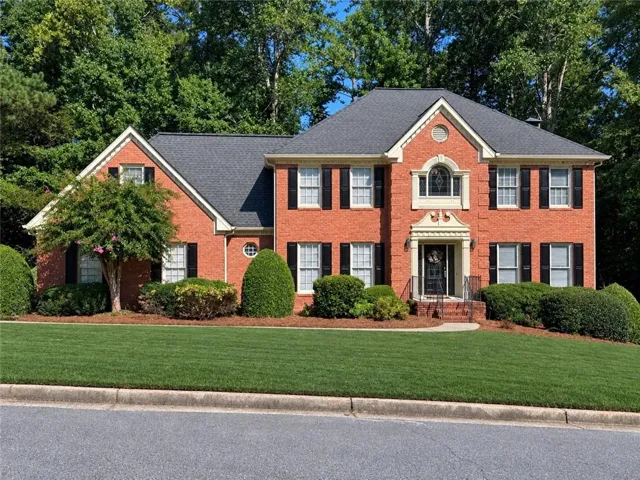 Brick exterior with a dark shingle roof, featuring a manicured lawn and mature landscaping