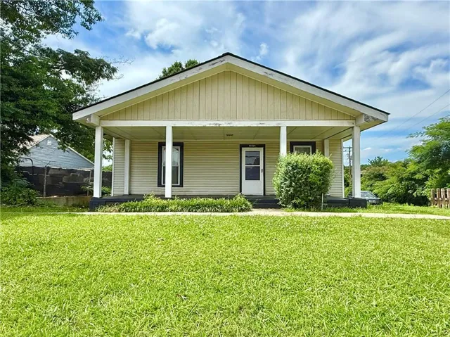Front exterior featuring light-colored siding, a covered porch with white columns, a dark roof, and a prominent front door