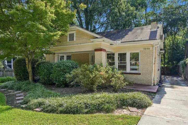 Brick exterior with shingle siding accents, covered front porch, established landscaping, and a side driveway