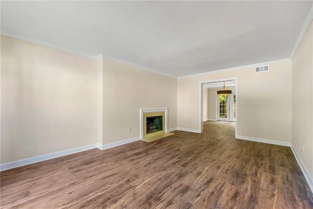 Unfurnished living room with wood finished floors, baseboards, ornamental molding, and visible vents