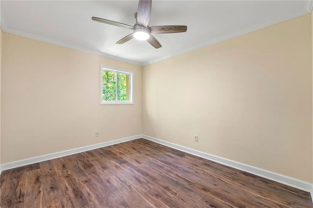 Unfurnished room with a ceiling fan, crown molding, baseboards, and dark wood finished floors