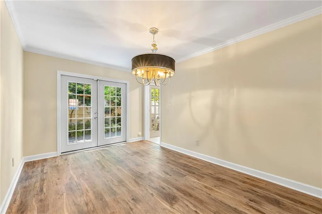 Empty room with a notable chandelier, baseboards, ornamental molding, french doors, and wood finished floors