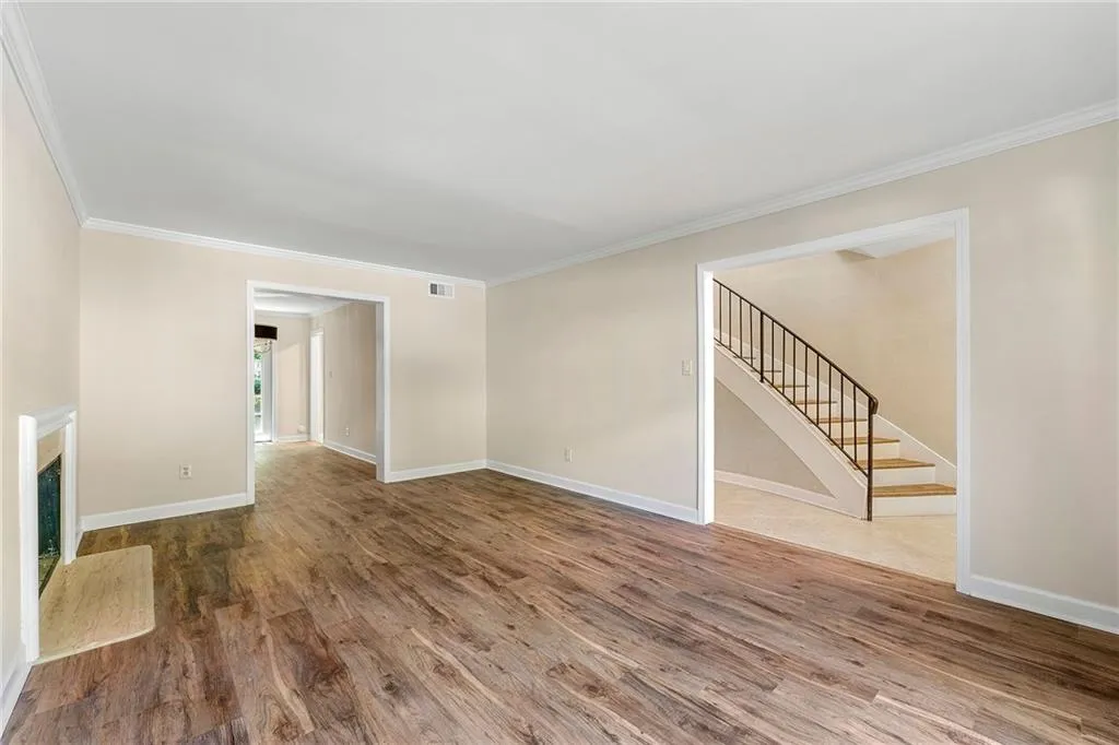 Unfurnished living room featuring stairs, baseboards, ornamental molding, and wood finished floors