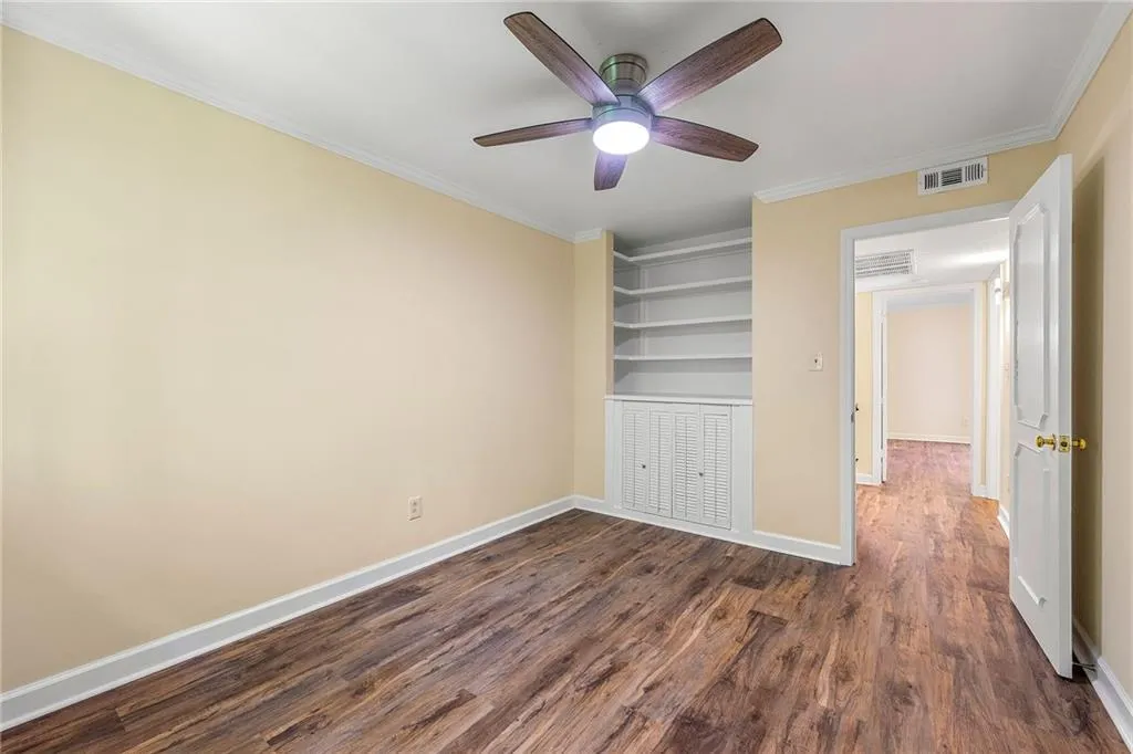Empty room featuring a ceiling fan, ornamental molding, visible vents, baseboards, and dark wood-style floors