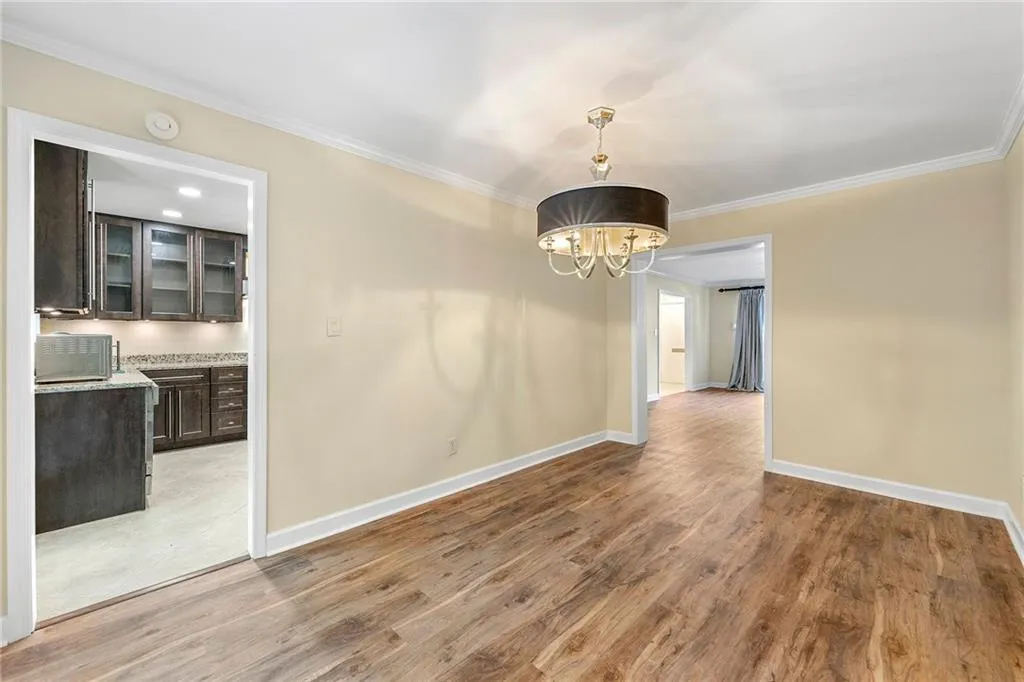 Unfurnished dining area with crown molding, wood finished floors, and a notable chandelier