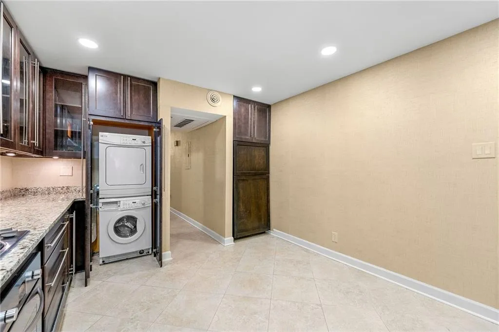 Laundry area with recessed lighting, light tile patterned floors, stacked washer and dryer, and baseboards