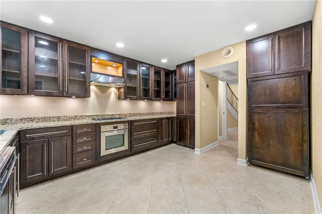 Kitchen with light stone counters, recessed lighting, dark brown cabinets, under cabinet range hood, and stainless steel appliances