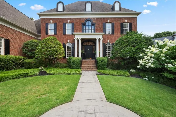Brick facade home featuring a prominent portico entrance with white columns, a dark front door, and a stone walkway