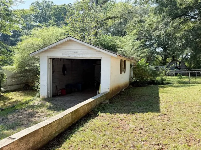 Detached garage structure with an open bay and side windows, surrounded by mature trees and a grassy area