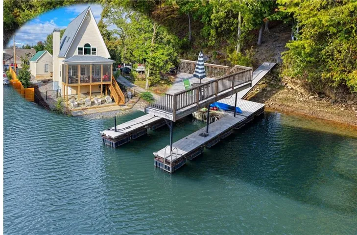 Waterfront property featuring a private dock with an elevated sitting area, a screened-in porch, and a lower-level patio