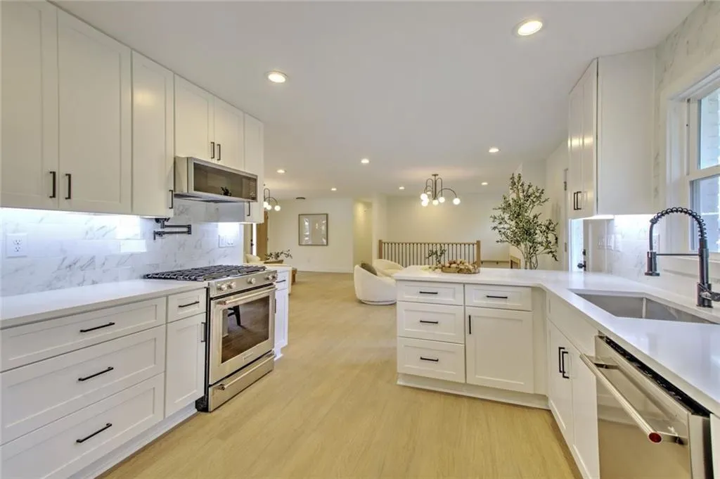 Kitchen with backsplash, appliances with stainless steel finishes, white cabinets, open floor plan, and recessed lighting