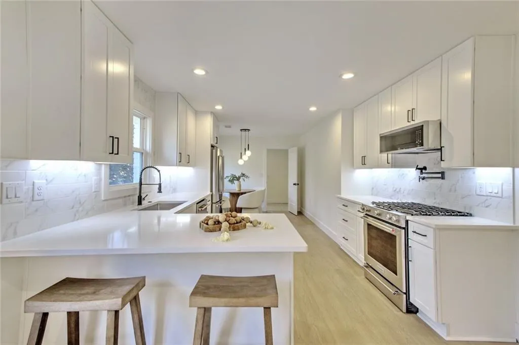 Kitchen featuring decorative backsplash, a breakfast bar area, stainless steel appliances, white cabinetry, and recessed lighting