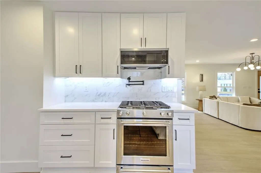 Kitchen featuring appliances with stainless steel finishes, white cabinetry, decorative backsplash, open floor plan, and light stone countertops