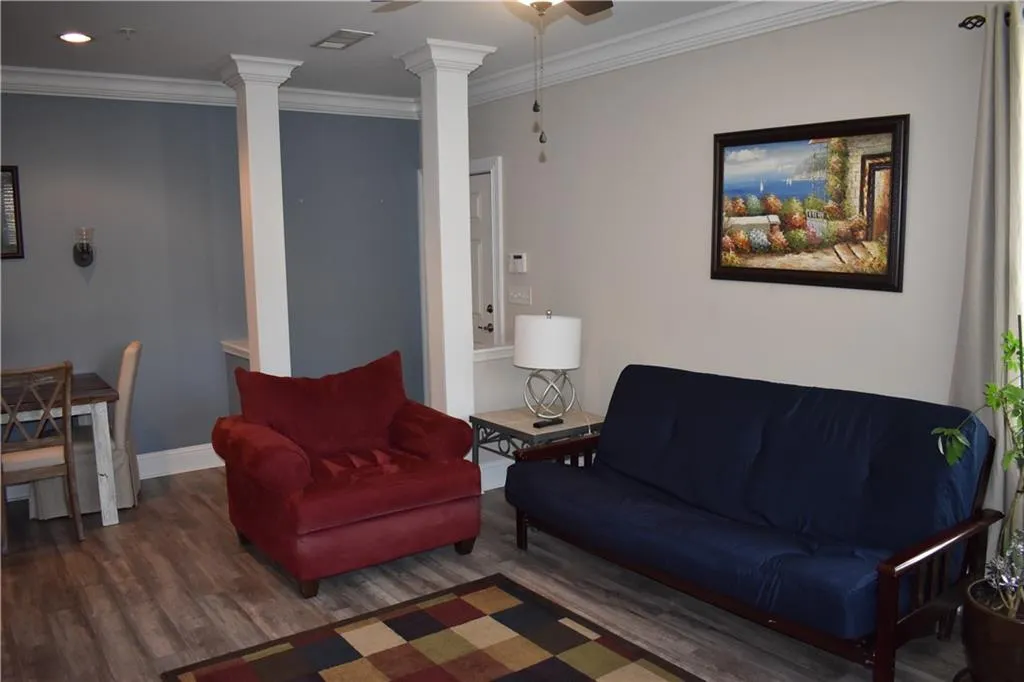 Living room with dark hardwood / wood-style flooring, ceiling fan, crown molding, and decorative columns